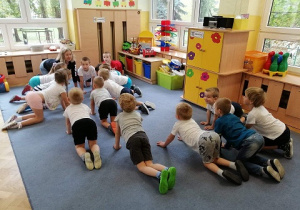 Dzieci z grupy Biedroneczki pięknie ćwiczą w klęku podpartym wykonując ćwiczenie pokazane przez nauczyciela